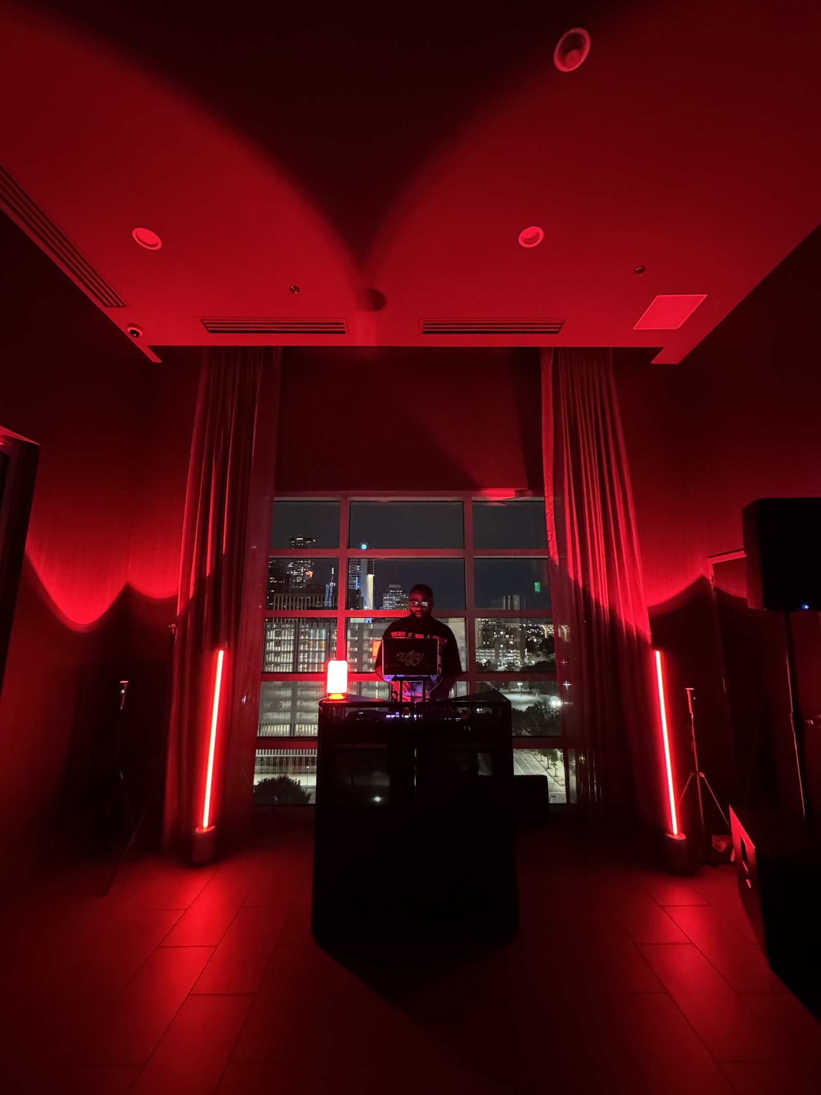 DJ FLYY performing at a red-lit rooftop event overlooking the skyline